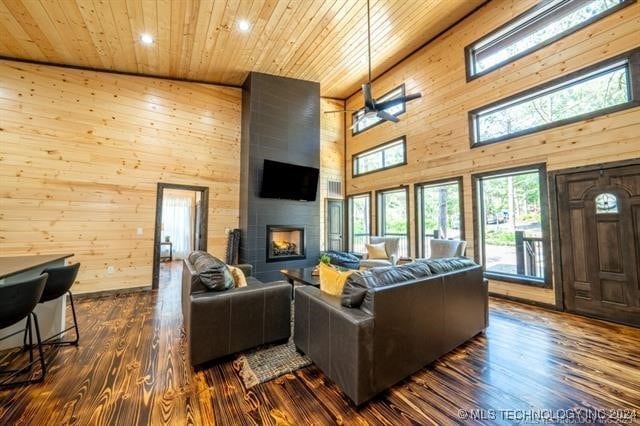 living room with wooden walls, dark hardwood / wood-style flooring, wood ceiling, high vaulted ceiling, and a large fireplace