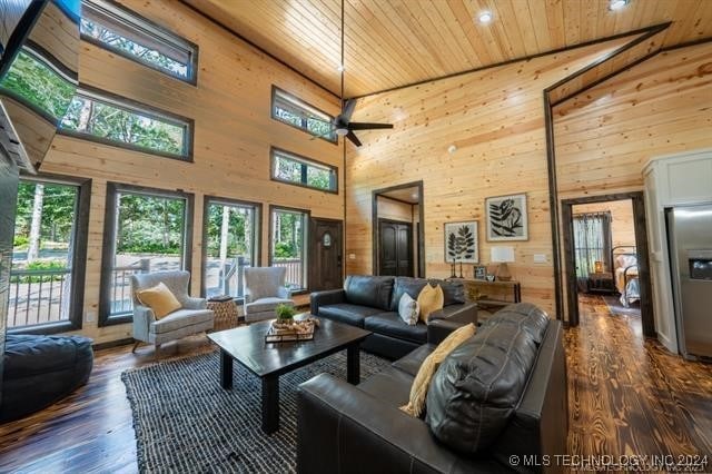 living room featuring ceiling fan, dark hardwood / wood-style floors, wood walls, and high vaulted ceiling