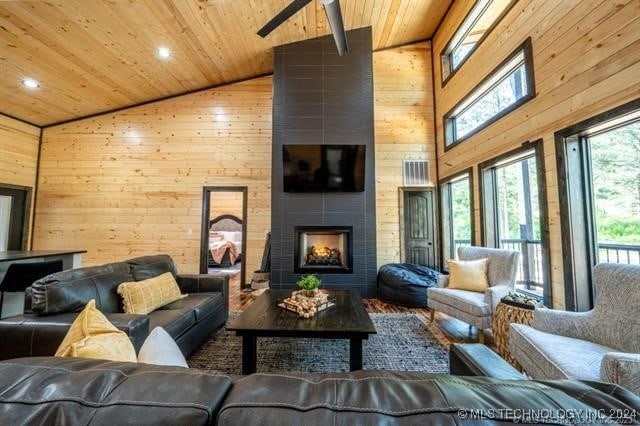 living room with a large fireplace, high vaulted ceiling, wood walls, wooden ceiling, and ceiling fan