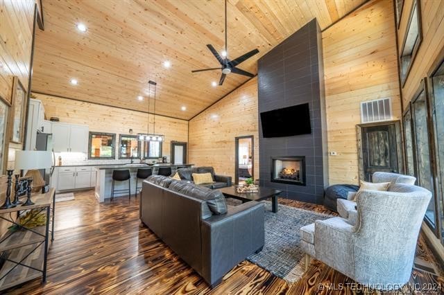 living room featuring ceiling fan, hardwood / wood-style floors, high vaulted ceiling, a tiled fireplace, and wood ceiling