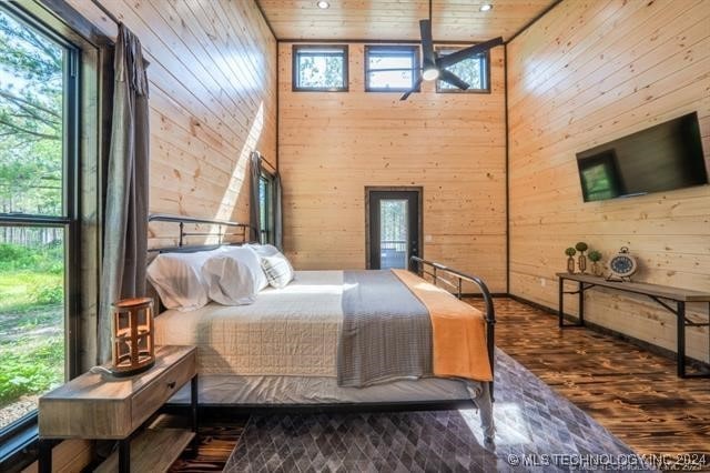 bedroom with wood walls, wood ceiling, dark wood-type flooring, and a towering ceiling