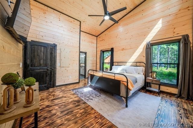 bedroom with high vaulted ceiling, wood walls, and hardwood / wood-style flooring