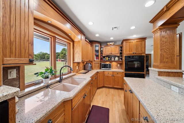 kitchen featuring sink, light hardwood / wood-style flooring, backsplash, double oven, and light stone counters