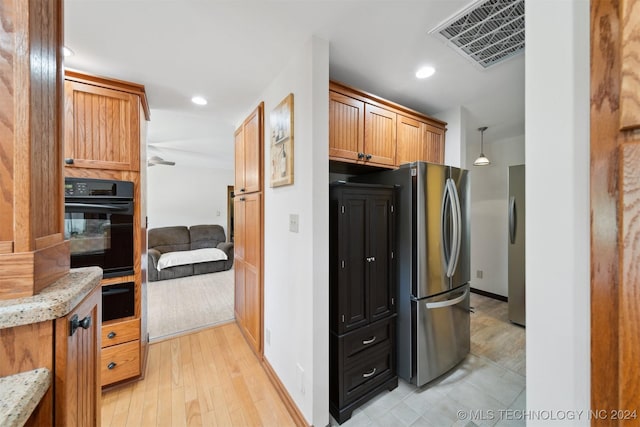 kitchen featuring hanging light fixtures, stainless steel fridge, light stone countertops, and oven