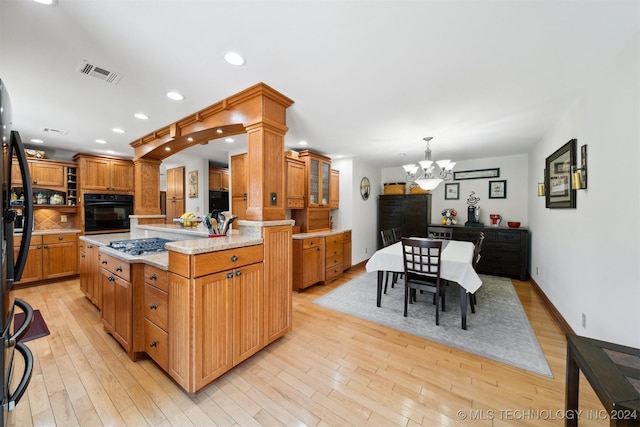 kitchen featuring tasteful backsplash, hanging light fixtures, a center island with sink, black oven, and light hardwood / wood-style floors