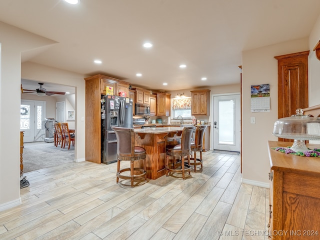 kitchen with ceiling fan, light stone countertops, light colored carpet, appliances with stainless steel finishes, and a kitchen breakfast bar