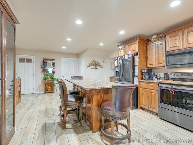 kitchen featuring stainless steel appliances, light wood-type flooring, a center island, light stone countertops, and a breakfast bar