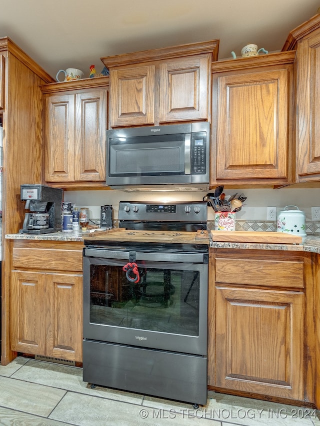 kitchen featuring light tile patterned flooring, stainless steel appliances, and light stone counters