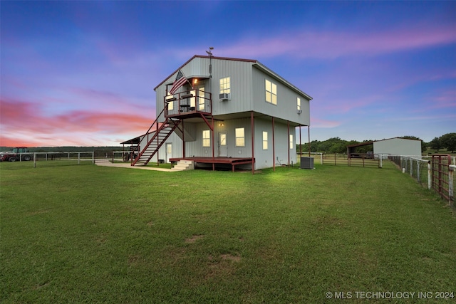 back house at dusk featuring a wooden deck, central AC, and a lawn