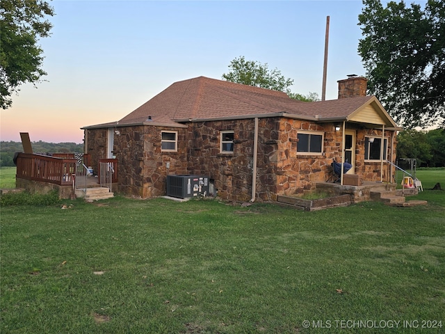 back house at dusk with central AC unit and a yard