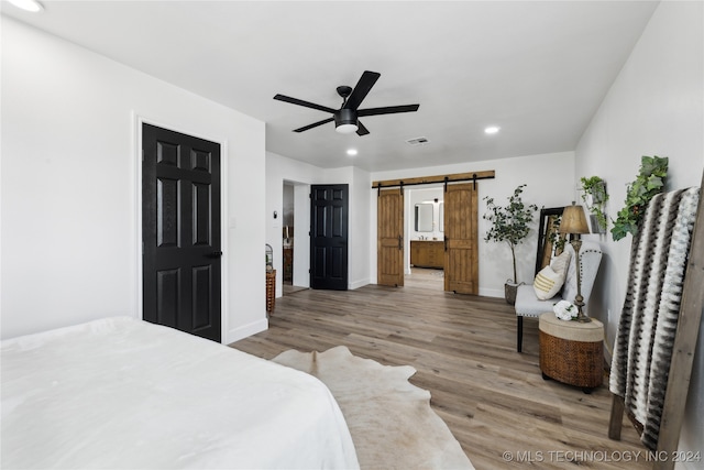 bedroom with hardwood / wood-style floors, a barn door, and ceiling fan