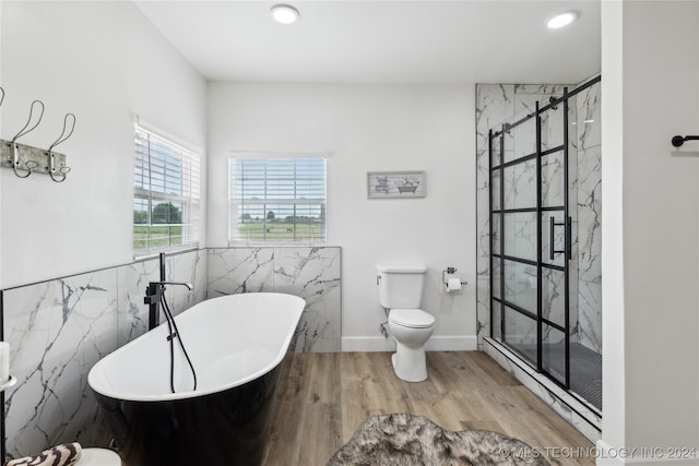 bathroom with tile walls, wood-type flooring, a tub to relax in, and toilet