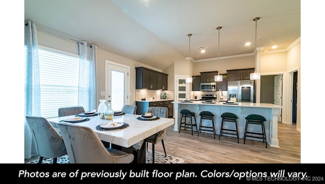 dining room with light wood-style floors, visible vents, ornamental molding, and vaulted ceiling