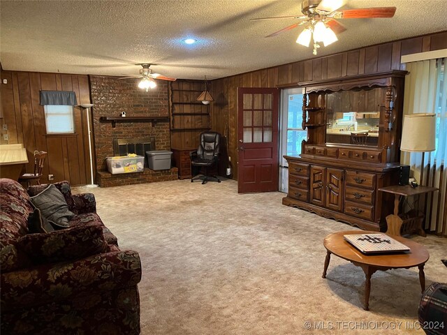 carpeted living room featuring a fireplace, a textured ceiling, wood walls, ceiling fan, and brick wall