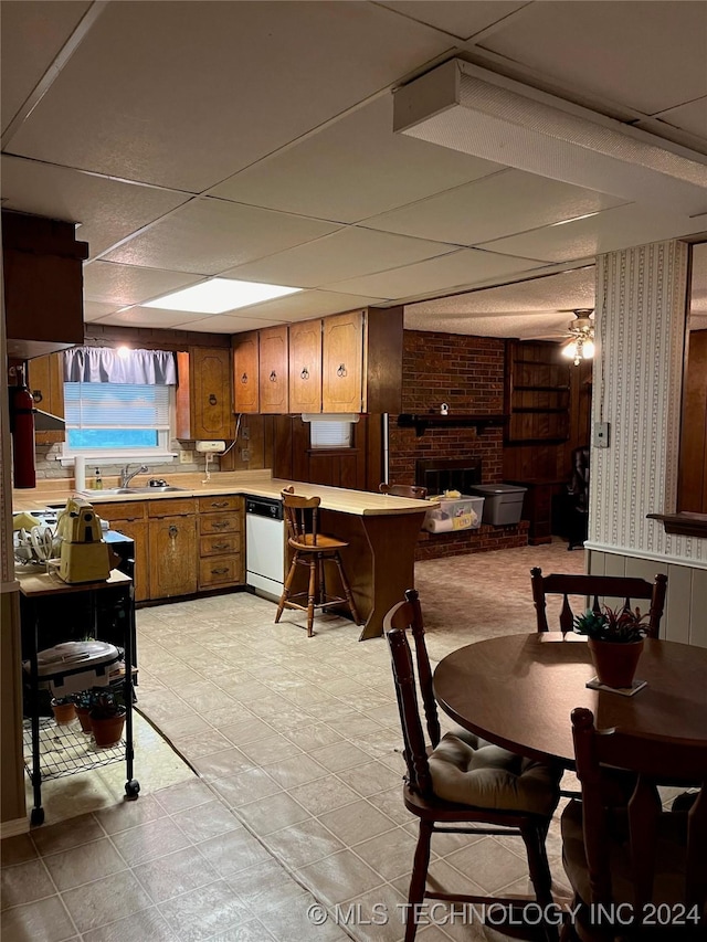 kitchen with brown cabinets, a sink, light countertops, a brick fireplace, and dishwasher