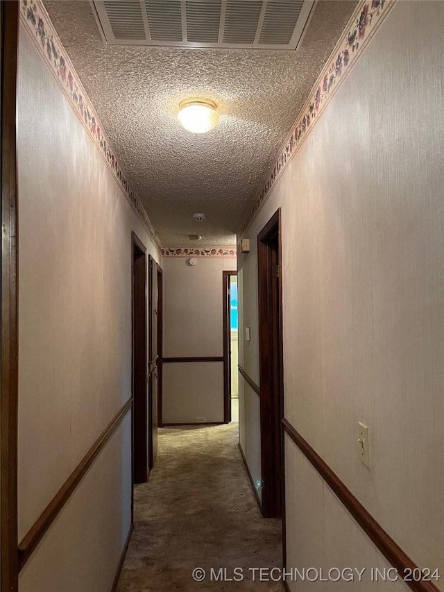 hallway featuring carpet, visible vents, and a textured ceiling