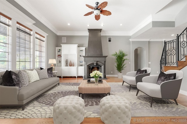 living room with a large fireplace, ceiling fan, light hardwood / wood-style floors, and ornamental molding