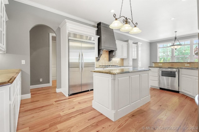 kitchen with appliances with stainless steel finishes, custom exhaust hood, white cabinets, light hardwood / wood-style floors, and a kitchen island