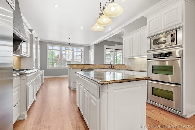 kitchen featuring light hardwood / wood-style flooring, ornamental molding, decorative light fixtures, a kitchen island, and white cabinetry