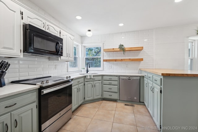 kitchen featuring wooden counters, light tile patterned floors, backsplash, stainless steel appliances, and sink