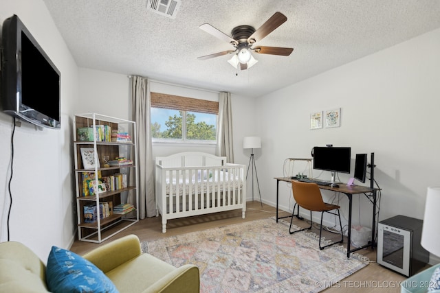 bedroom with a crib, ceiling fan, a textured ceiling, and light hardwood / wood-style flooring