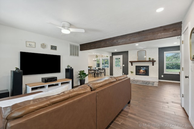 living room featuring dark hardwood / wood-style floors, a brick fireplace, beam ceiling, brick wall, and ceiling fan