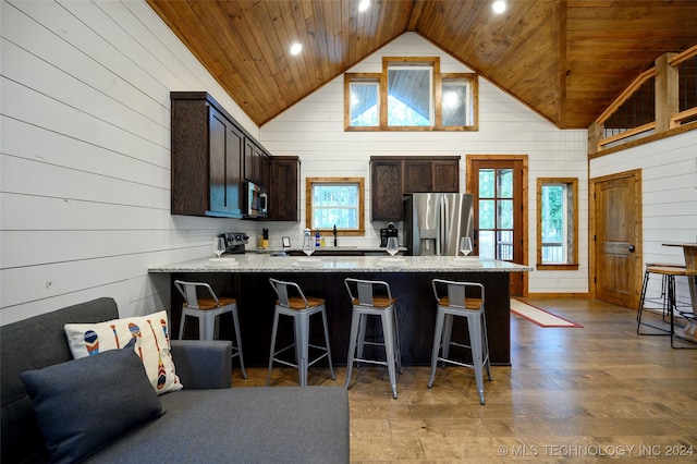 kitchen with wood ceiling, appliances with stainless steel finishes, a kitchen breakfast bar, dark brown cabinetry, and light stone countertops