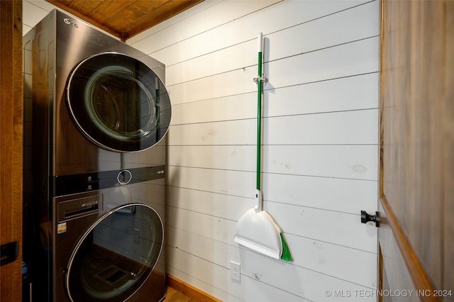 clothes washing area with stacked washer and dryer, wooden ceiling, and wood walls