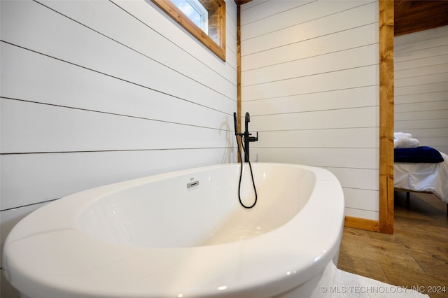 bathroom with a bathtub, hardwood / wood-style floors, and wood walls