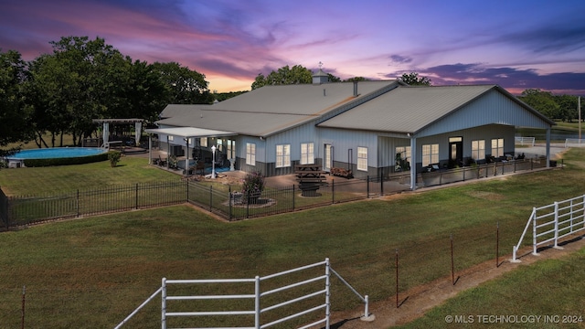 back house at dusk featuring a patio area, a yard, and a fenced in pool