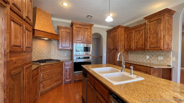 kitchen with appliances with stainless steel finishes, ornamental molding, custom range hood, sink, and wood-type flooring