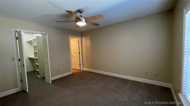 unfurnished bedroom with ceiling fan, dark carpet, a walk in closet, and a closet