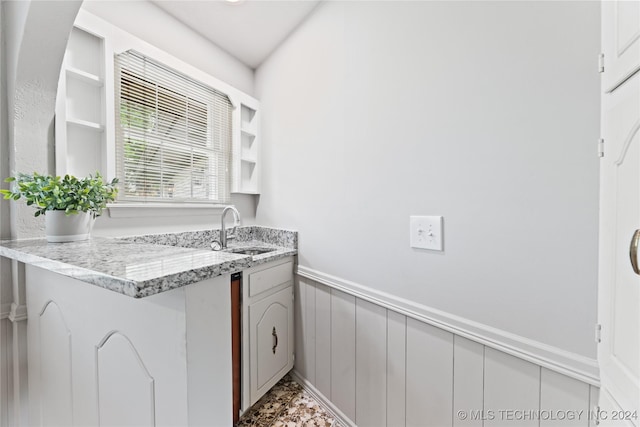 kitchen with light stone counters, white cabinetry, and sink