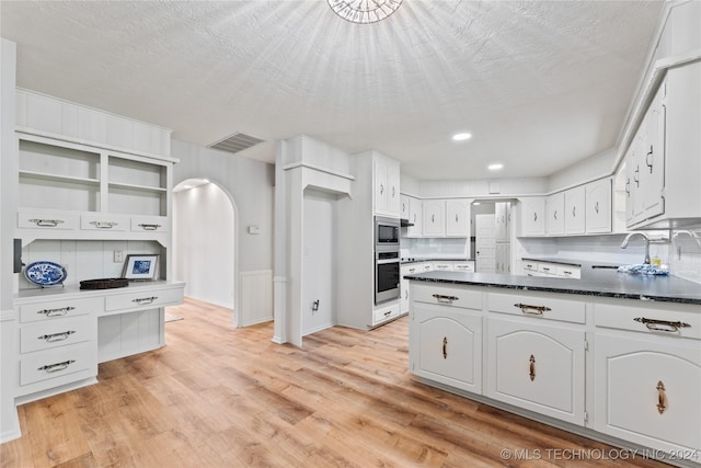 kitchen with appliances with stainless steel finishes, white cabinetry, decorative backsplash, a textured ceiling, and light hardwood / wood-style flooring