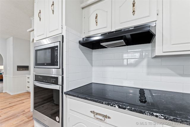 kitchen with appliances with stainless steel finishes, white cabinets, backsplash, light hardwood / wood-style floors, and exhaust hood