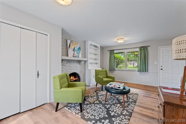 sitting room with light hardwood / wood-style floors, built in features, a brick fireplace, and brick wall