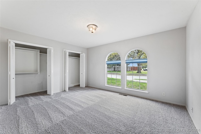 unfurnished bedroom with two closets and light colored carpet