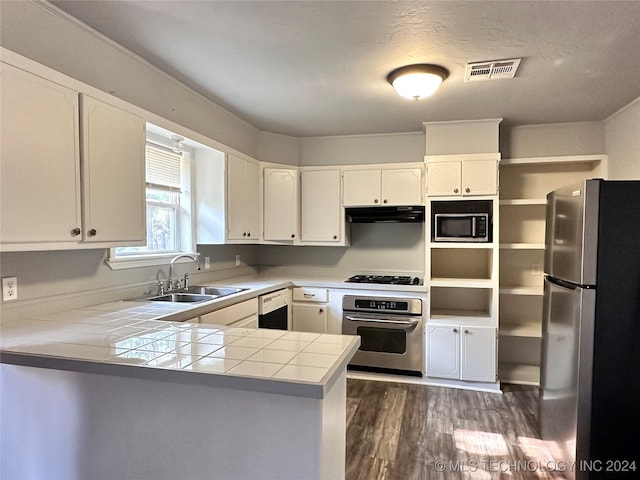 kitchen with dark hardwood / wood-style flooring, white cabinets, appliances with stainless steel finishes, tile countertops, and kitchen peninsula