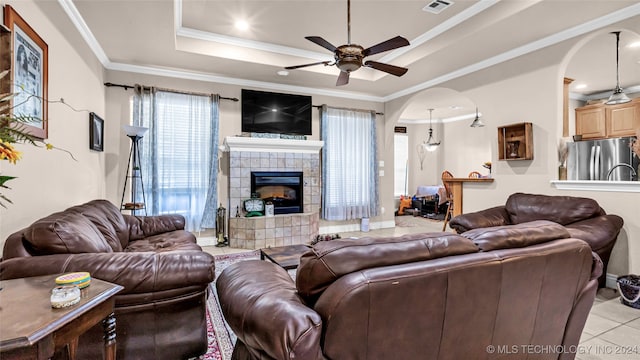 tiled living room featuring ornamental molding, a fireplace, ceiling fan, and a raised ceiling