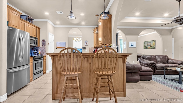 kitchen with crown molding, kitchen peninsula, ceiling fan with notable chandelier, stainless steel appliances, and a kitchen bar