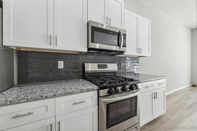 kitchen with stainless steel appliances, white cabinets, light stone countertops, tasteful backsplash, and light hardwood / wood-style floors