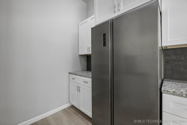 kitchen featuring stainless steel fridge, white cabinets, light wood-type flooring, and light stone counters