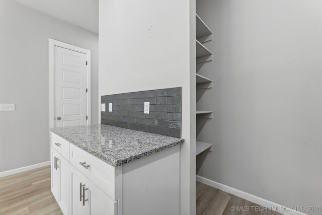 kitchen featuring light wood-type flooring, white cabinets, light stone counters, and backsplash