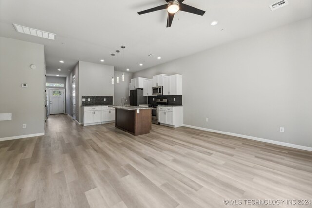 kitchen with pendant lighting, appliances with stainless steel finishes, an island with sink, backsplash, and light hardwood / wood-style flooring