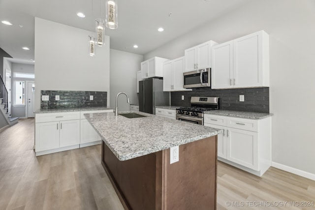 kitchen with tasteful backsplash, light wood-type flooring, stainless steel appliances, sink, and decorative light fixtures