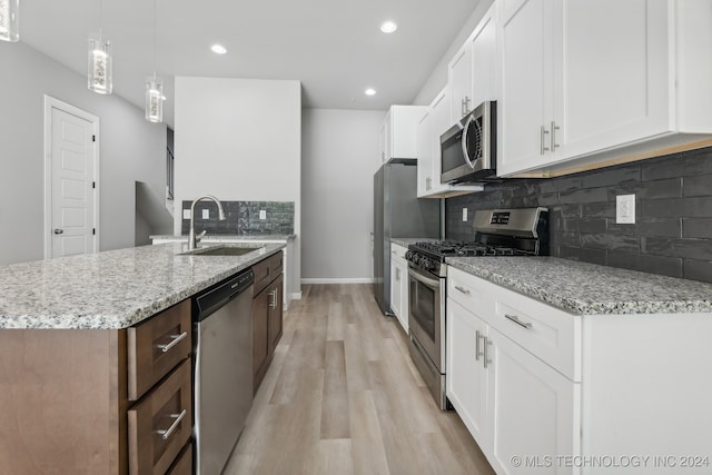 kitchen with tasteful backsplash, appliances with stainless steel finishes, light hardwood / wood-style floors, white cabinets, and decorative light fixtures