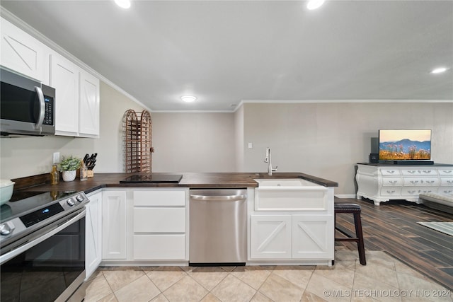 kitchen with kitchen peninsula, appliances with stainless steel finishes, ornamental molding, sink, and white cabinetry