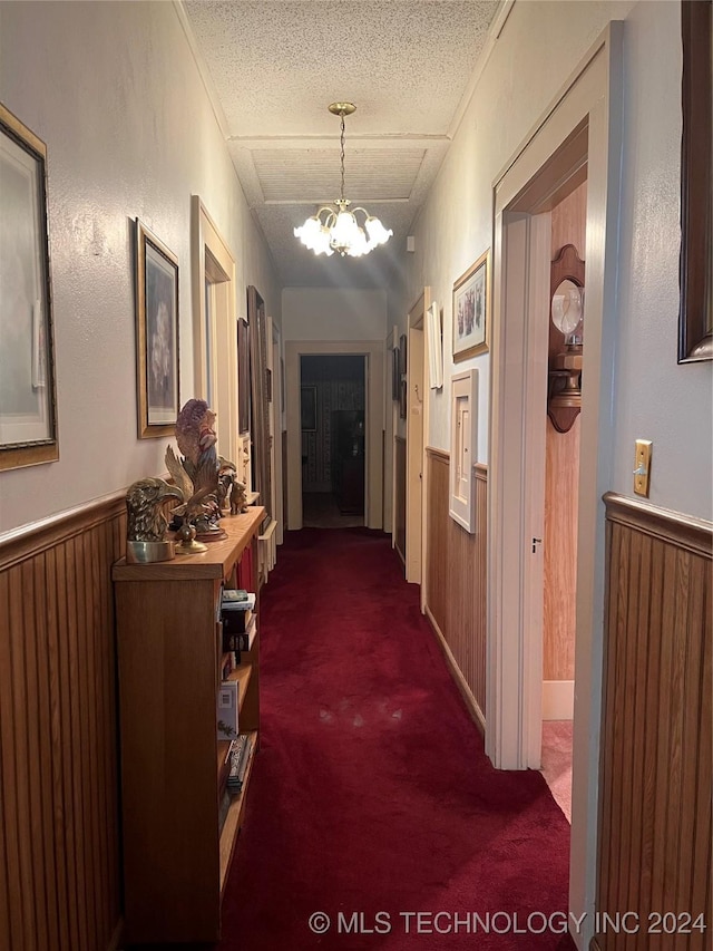 hallway featuring wood walls, dark colored carpet, and a chandelier