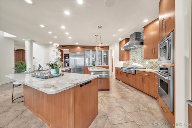 kitchen featuring built in appliances, a spacious island, wall chimney range hood, backsplash, and ornate columns