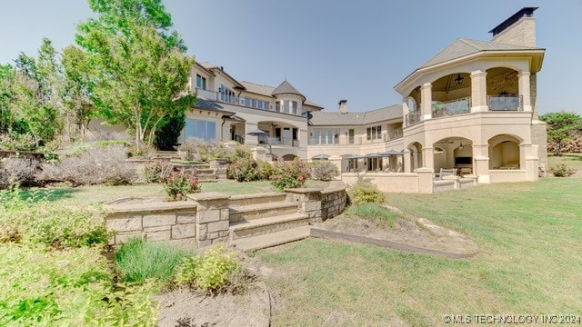 back of property with a balcony, a chimney, and a yard